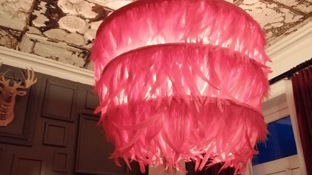 Lustre original à plumes roses suspendu dans une pièce à la décoration vintage, avec un plafond orné et des moulures