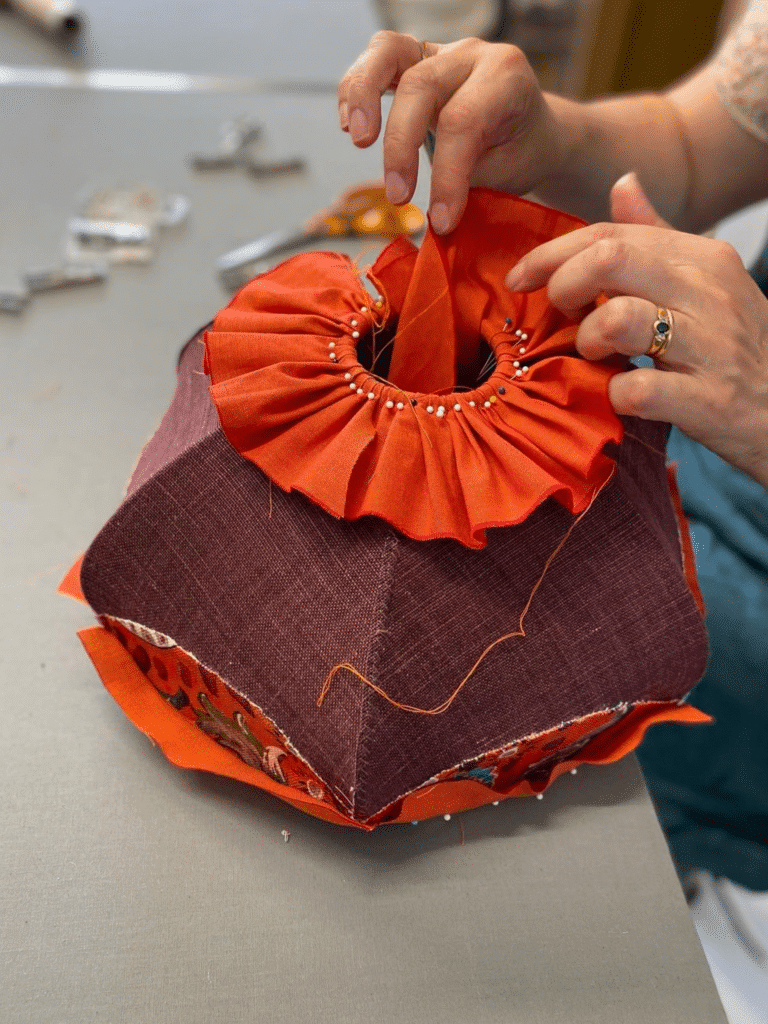 Artisan en train de fabriquer un abat-jour en tissu avec des finitions plissées de couleur orange