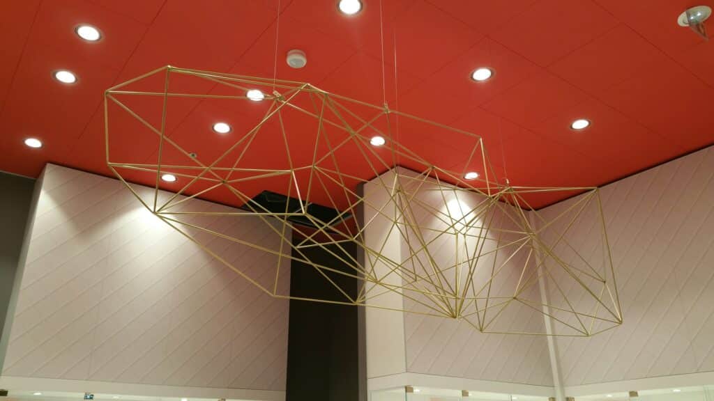 Suspension design en structure métallique dorée aux formes géométriques, installée dans un intérieur moderne