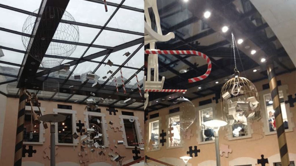 Installation artistique suspendue sous une verrière, composée de cages métalliques et d’éléments décoratifs en forme de puzzle